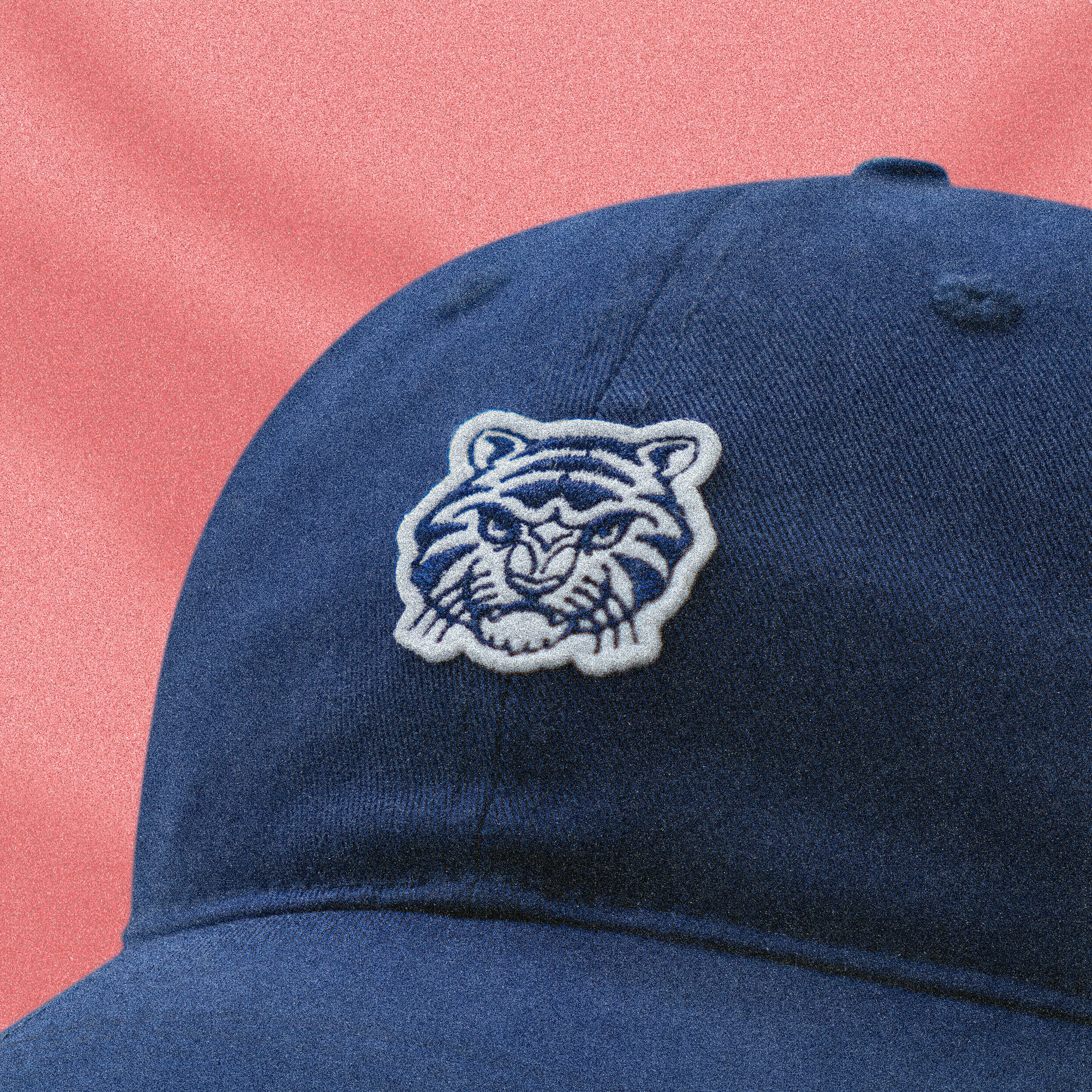 Navy blue cap with a tiger logo on a pink background