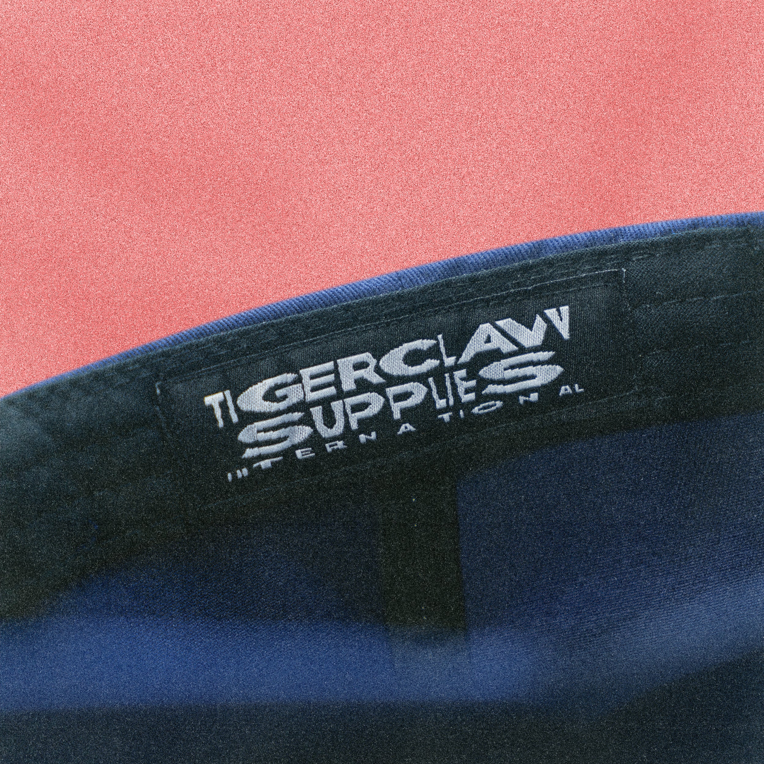 Close-up of a Tigerclaw Supplies International label on a blue product with a pink background