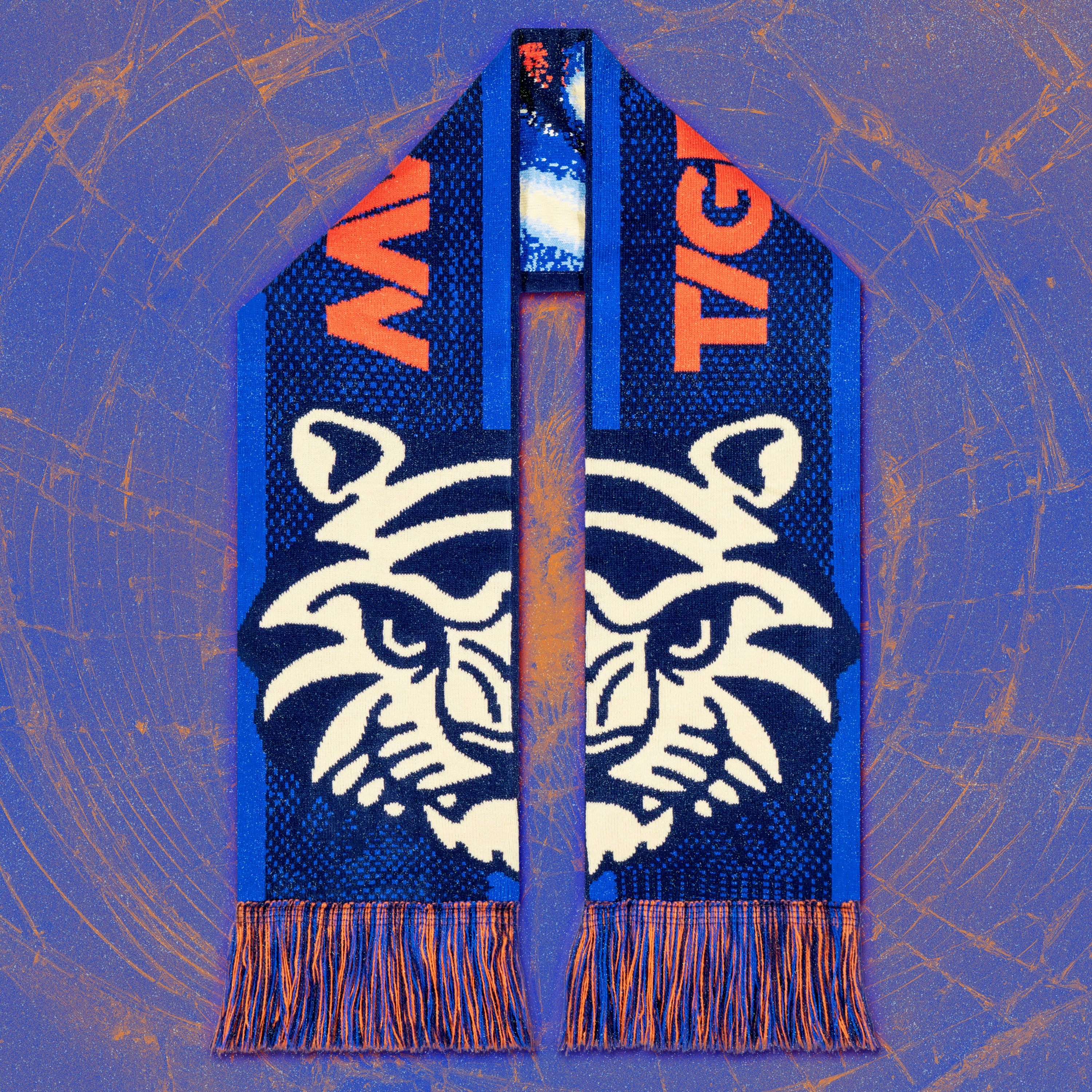 Blue football scarf with bold orange “TIG” lettering and a large white tiger face motif split down the middle, arranged vertically with orange-and-blue fringes against a textured blue and orange background.