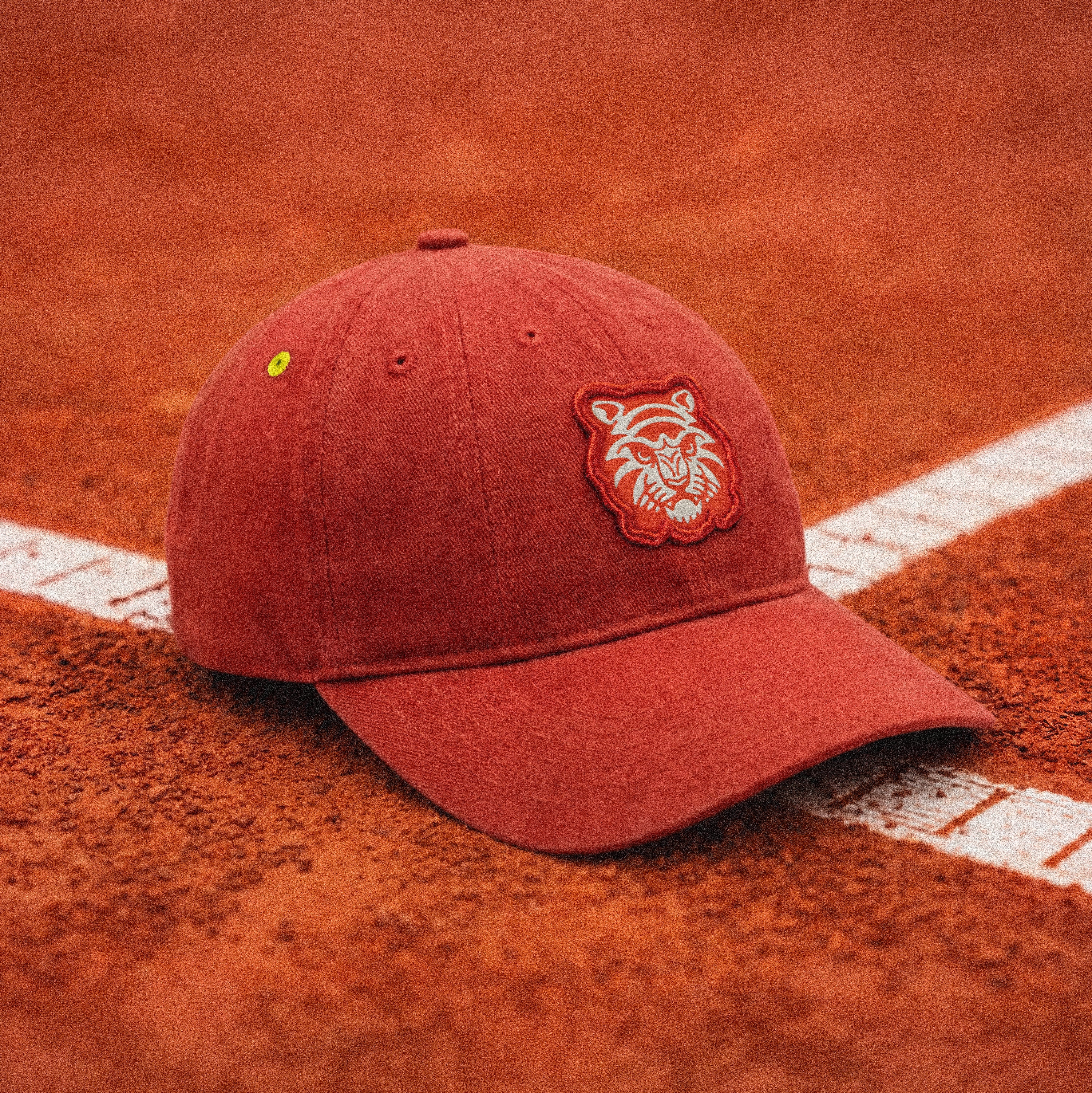 Clay Legacy tennis cap resting on a clay court featuring Tigerclaw tiger embroidery and signature neon yellow eyelet