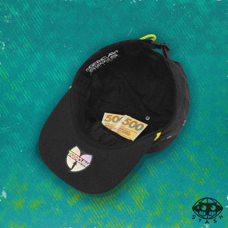 nside view of a black 6-panel cap showing hidden stash pocket with two 500 bills tucked in, set against a textured teal background. Features a Tigerclaw holographic sticker and “STASH” icon.
