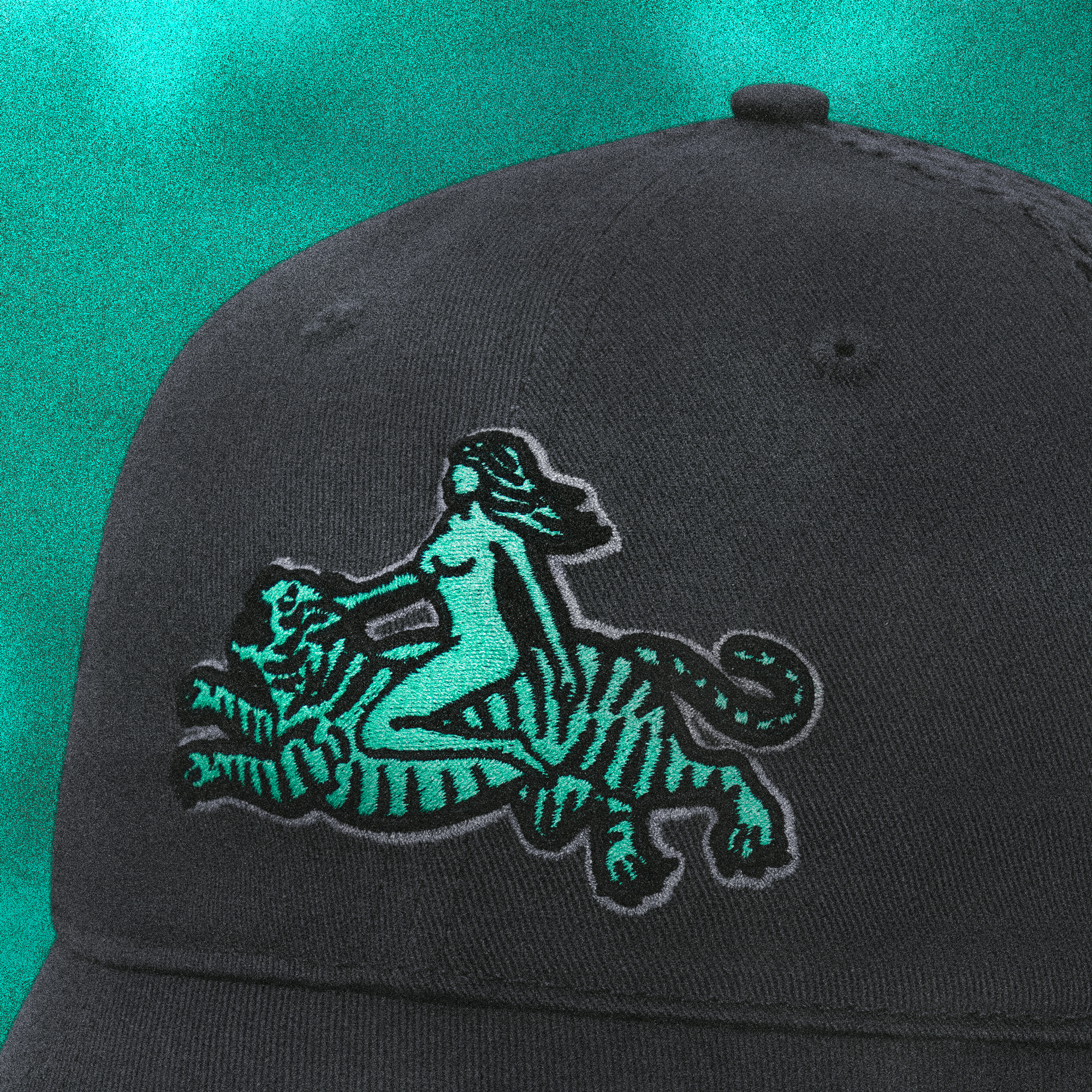 Close-up front view of the Tigerclaw Wild Ride trucker cap in dark grey, featuring turquoise embroidery of a woman riding a tiger.