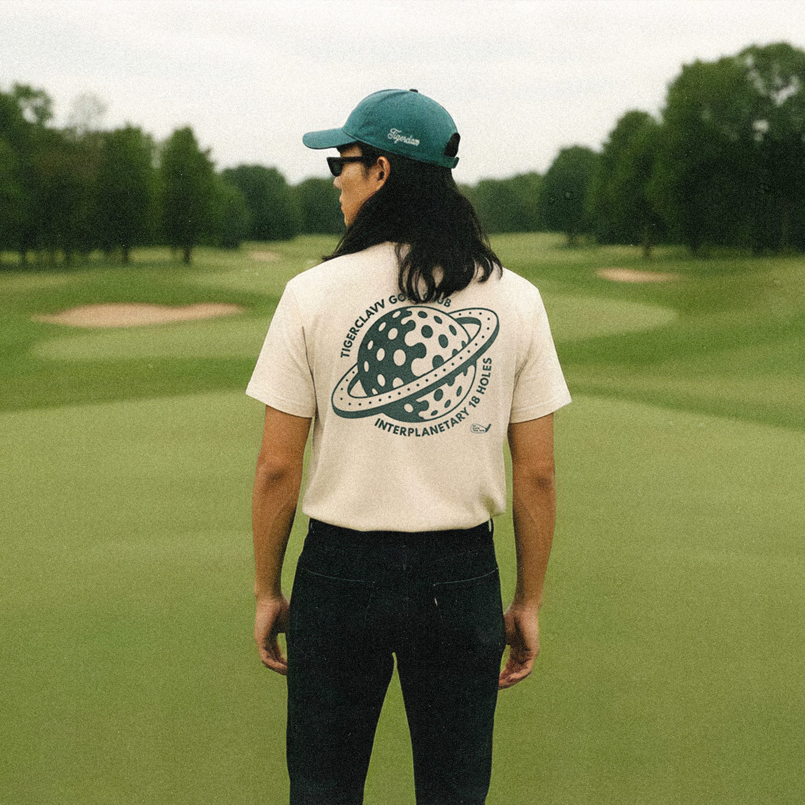 Model wearing Tigerclaw Golf Club Tee with back print, standing on a golf course