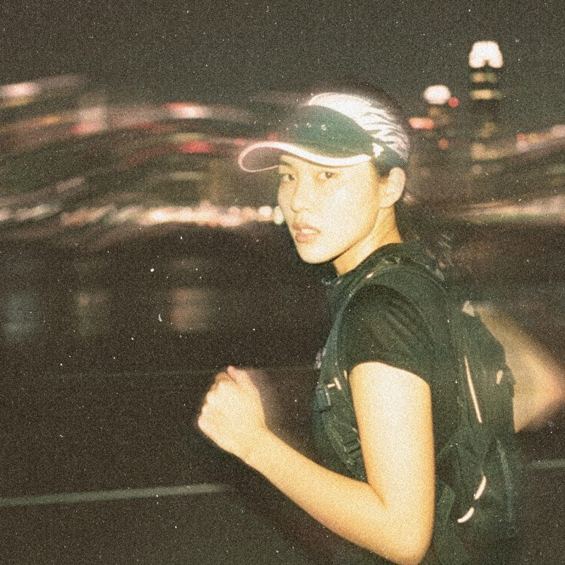 Runner in motion wearing the Tigerclaw LUMEN8 reflective 8-panel cap at night with city lights in the background.
